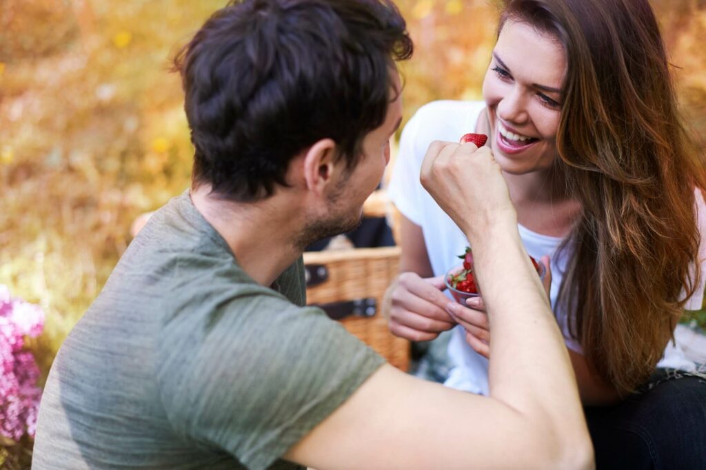 Romantic couple on a picnic, man feeding woman strawberries while laughing